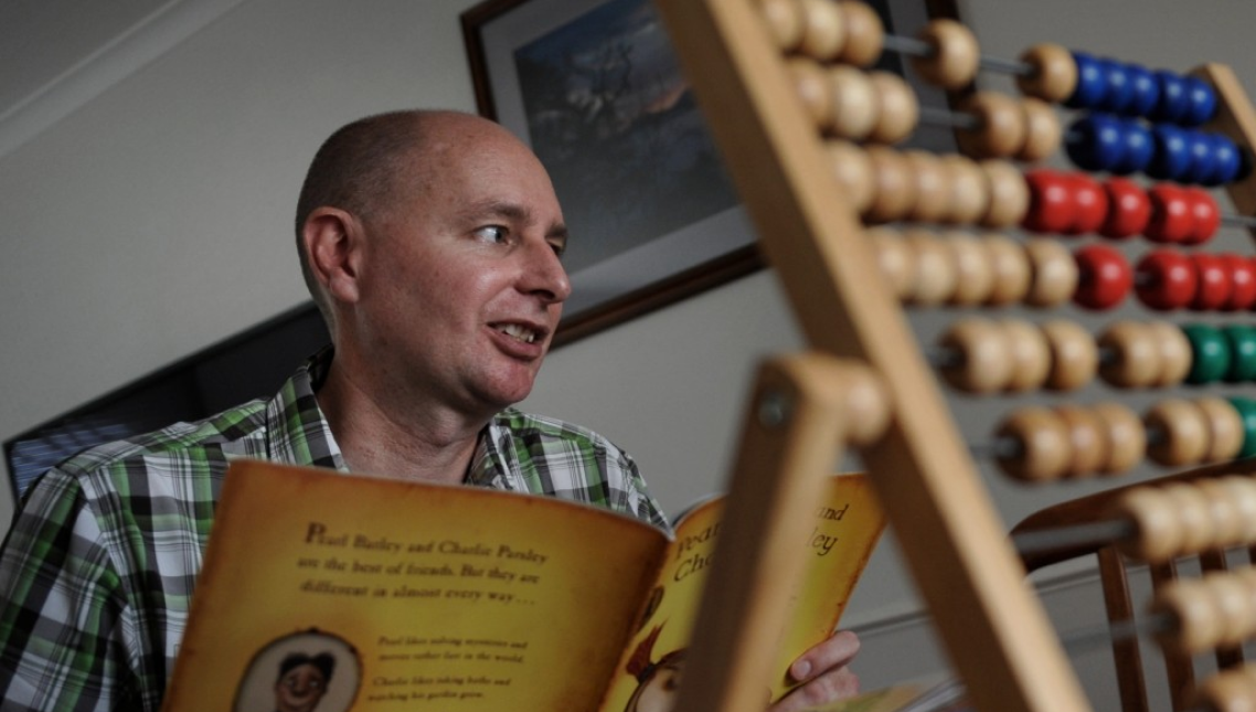 A man reading a children's book jovially with a toy abacus in the foreground